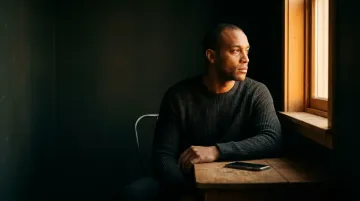 Person sitting alone in dim room with warm light from window thinking about narcissistic abuse syndrome.