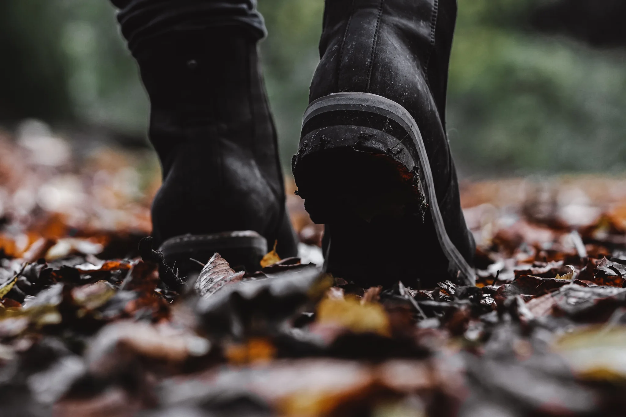 Boots mid-stride on a leaf-covered forest path.