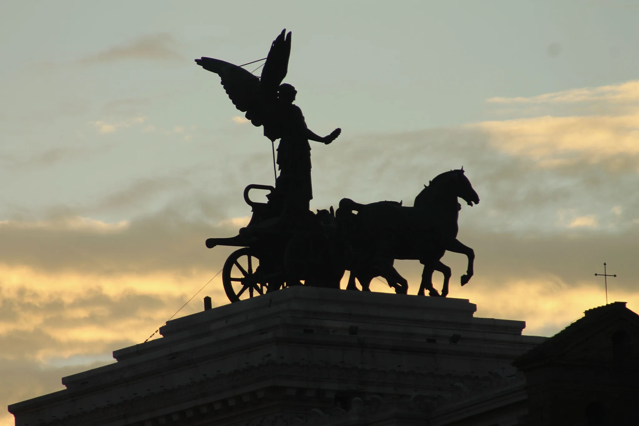 A bronze chariot statue silhouetted against a sunset sky.