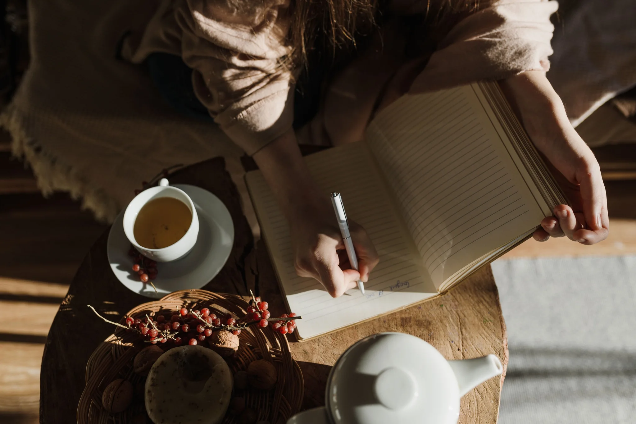 A hand writing in an open notebook beside a cup of tea.
